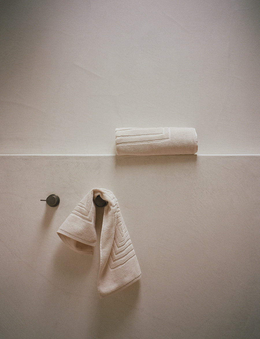 alt="Laze Res bath and hand towels from organic set hanging in serene, sunlit bathroom"
